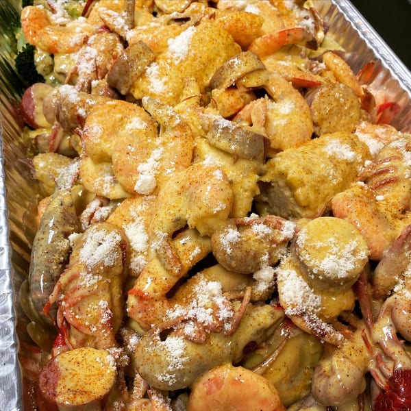 Cajun seafood boil with shrimp, sausage, and potatoes, topped with cheese and seasoning in a foil pan.