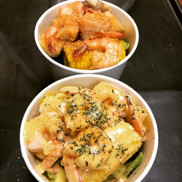 Two Louisiana Shack bowls of Cajun shrimp, one with corn and the other with creamy sauce and herbs.