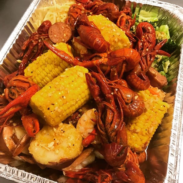 Louisiana Shack's Cajun seafood boil with crawfish, corn, sausage, shrimp, and broccoli in a foil pan.